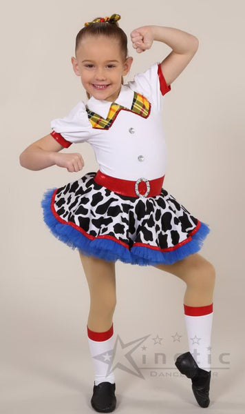 A young girl modeling a Jessie Cow costume, featuring a white short-sleeve top with red trim and a plaid collar, a black and white cow-print skirt with a blue tulle hem, a red belt, and white knee-high socks with red trim.