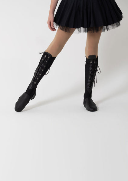 lower half of a woman wearing a tulle skirt with black jazz shoes on and lace up spats going to the knee