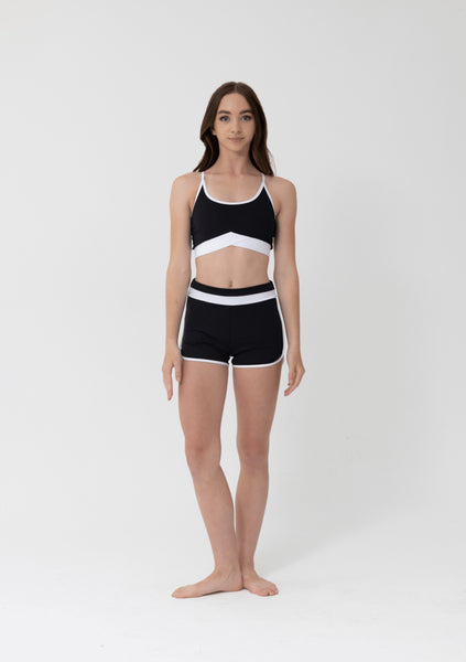 Person wearing a black and white thin strap crop top and and shorts sports set  on a white background