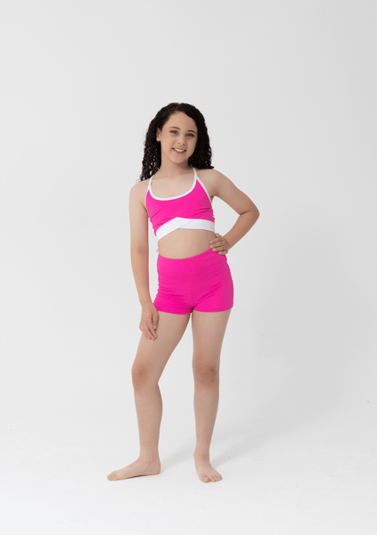 Young girl wearing a pink sports bra and shorts set on a white background