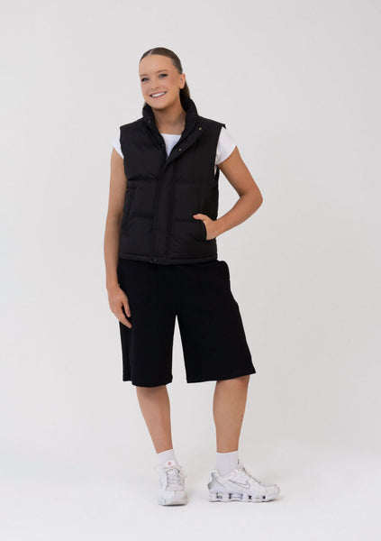 Person wearing a black sleeveless vest and black shorts on a white background