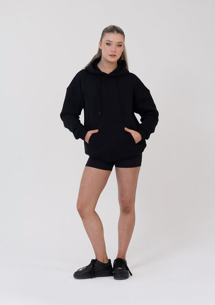 Person wearing a black hoodie and shorts set on a white background