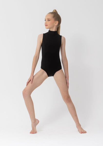 A young girl with blonde hair in a ponytail poses in a sleeveless black mock-neck leotard against a plain light gray studio background.
