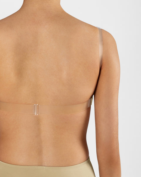 Rear view of a model wearing a transparent adhesive underwire bra with a hook-and-loop closure band on a light gray background.