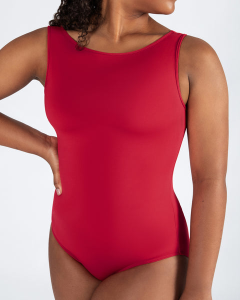 A woman wearing a sleeveless red one-piece swimsuit or bodysuit against a plain light gray studio background.