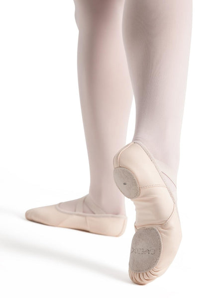 A pair of beige leather ballet shoes on a person's feet, in a ballet position.