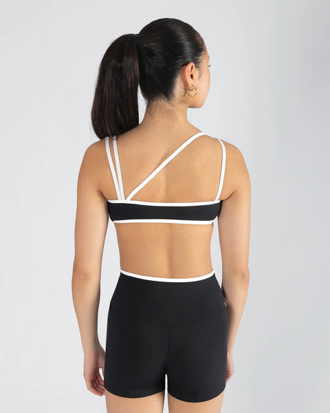 Woman wearing a black and white sports bra and shorts on a gray background