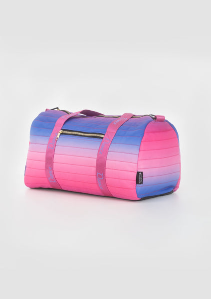 A Studio 7 Vivid Duffel Bag with ombre design, featuring pink to blue gradient, with two external gold zipped pockets and a shoulder strap.